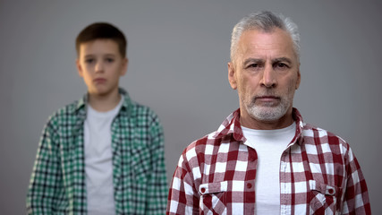 Aged male looking to camera, little boy standing behind, retirement age increase