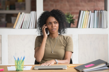 Frowning african businesswoman having unpleasant conversation on phone