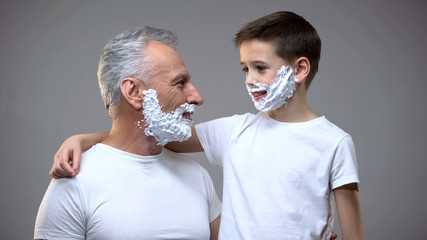Happy grandfather and grandson in shaving foam looking at each other, having fun