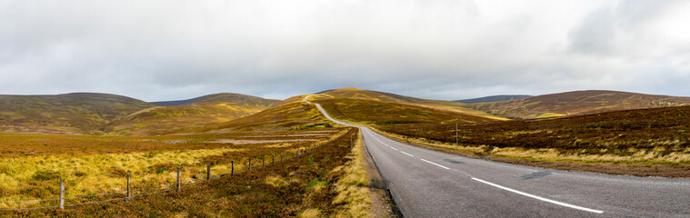 A scenic highway through bright yellow and brown highlands during autumn season in Cairngorms national park, Scotland