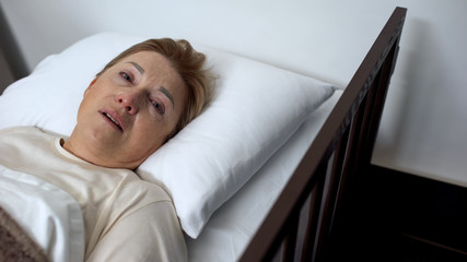 Terminally ill senior lady crying and looking into camera, lying in hospice bed