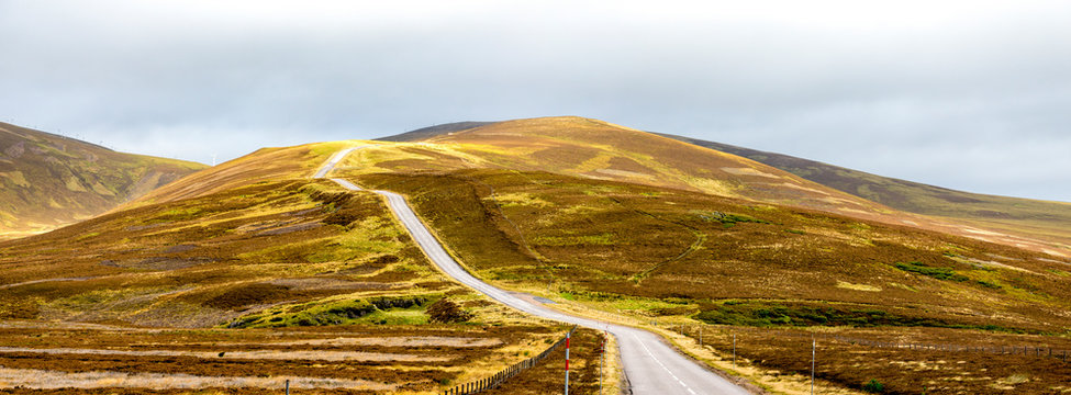 A scenic highway through bright yellow and brown highlands during autumn season in Cairngorms national park, Scotland
