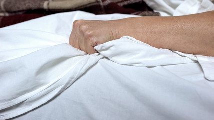 Terminally-ill woman clenching bedsheets feeling terrible pain, death convulsion