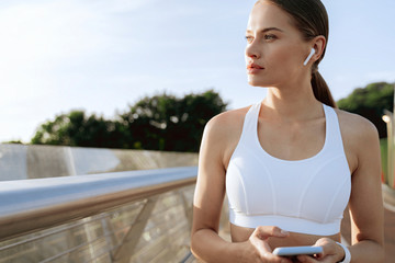 Young sportive lady in headphones with mobile