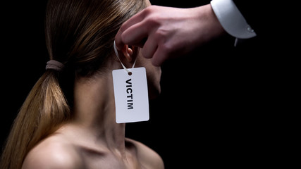 Male hand putting victim label on female ear, humiliation and bullying, close-up - obrazy, fototapety, plakaty