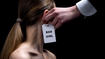 Male hand putting bad girl label on female ear, stereotypes about women behavior