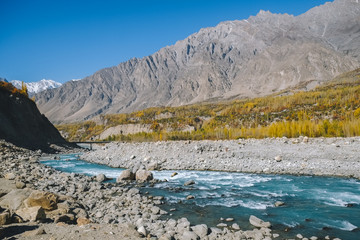 Turquoise blue river flowing through Hunza Nagar valley in autumn season with a view of Karakoram mountain range. Gilgit Baltistan, Pakistan.