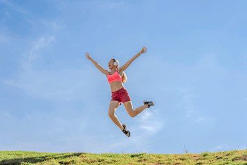 Joyful sportive lady jumping up on green hill