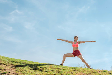 Harmonious lady practicing yoga warrior asana on hill