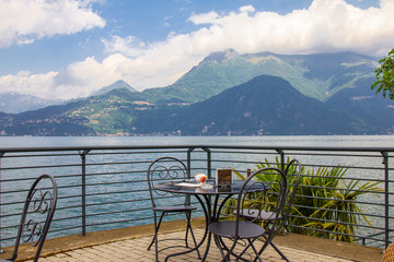 Beautiful view from terrace cafe of the overlooking the high mountains and shore lake Como. Empty wicker restaurant chairs are waiting for guests in a chic restaurant in the ancient city of Varenna.