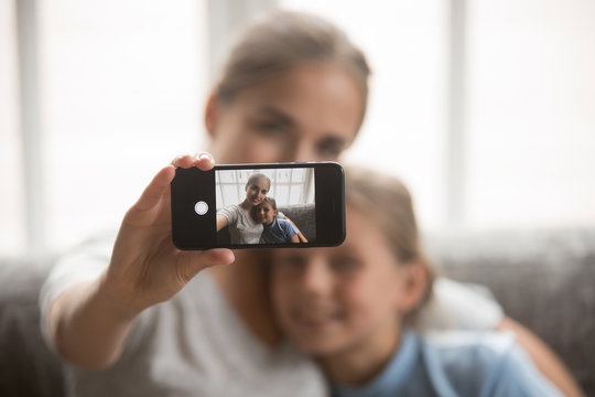 Mother and daughter embracing making selfie view through mobile screen