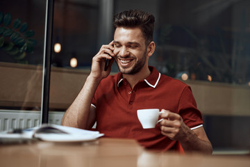 Young man talking at smartphone in cafe