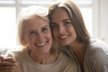 Middle aged mother grown up daughter embracing looking at camera