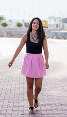 Obraz premium Smiling young woman with pink skirt and black shirt walking. Healthy lifestyle. Urban lifestyle