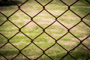 Naklejka premium The close up of brown wire fence (barricade) which is hardly rusted in blurred background (meadow).