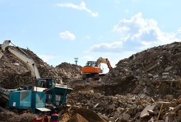 Excavator loads construction waste into reinforced concrete mobile shredder for crushing, recycling of construction mixed waste. Broken concrete recycling at industrial landfill. Screening plant