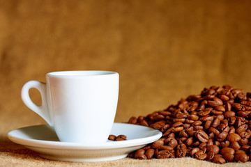 White cup and coffee beans on a blurred background.