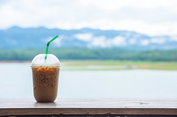 Glass of cold espresso coffee on the table Background blurry views sky water and mountain.
