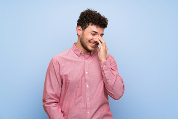 Man with curly hair over isolated blue wall smiling a lot