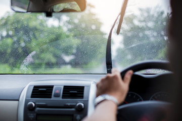 Selective focus to man driving a car with rain droplet on windshield and wiper. Windshield wipers from inside of car, season rain.