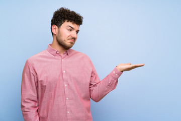 Man with curly hair over isolated blue wall holding copyspace with doubts