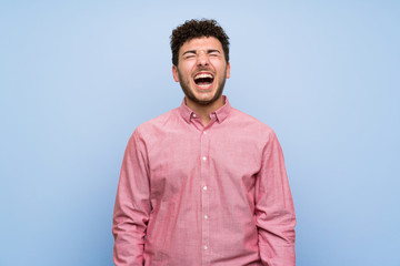 Man with curly hair over isolated blue wall shouting to the front with mouth wide open