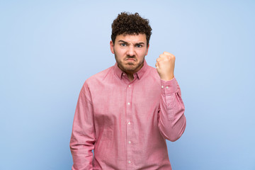 Man with curly hair over isolated blue wall with angry gesture