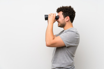 Man with curly hair over isolated wall with black binoculars