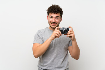 Man with curly hair over isolated wall holding a camera