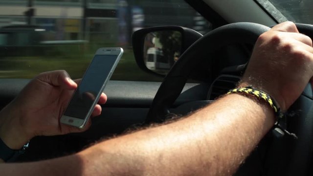 Turkey, Antalya , 3 August. A man driving a car, holding the steering wheel with one hand, and at the same time looking for something in the phone, visible only hands. The concept of dangerous situati