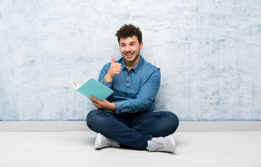 Young man sitting on the floor holding and reading a book