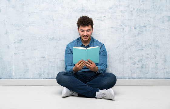Young man sitting on the floor holding and reading a book