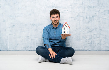 Young man sitting on the floor holding a little house