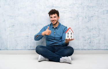 Young man sitting on the floor holding a little house