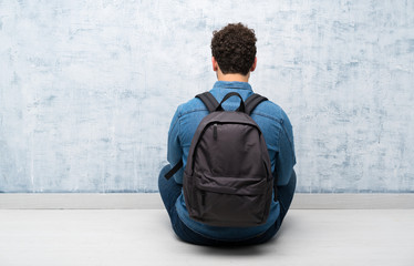 Young man sitting on the floor with backpack