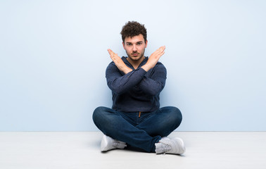 Young man sitting on the floor making NO gesture