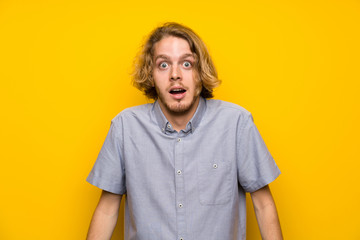 Blonde man over isolated yellow background with surprise facial expression