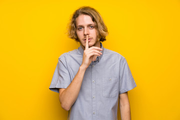 Blonde man over isolated yellow background showing a sign of silence gesture putting finger in mouth