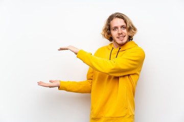Blonde man with  sweatshirt over white wall holding copyspace to insert an ad