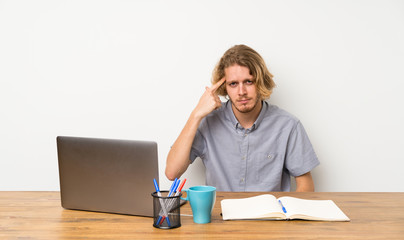 Blonde man with a laptop making the gesture of madness putting finger on the head