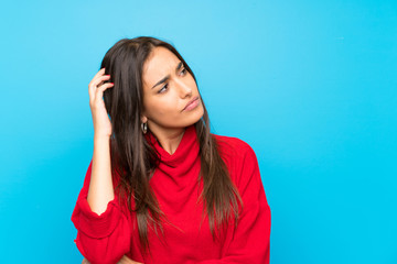 Young woman with red sweater over isolated blue background having doubts and with confuse face...