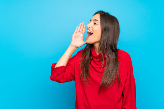 Young woman with red sweater over isolated blue background shouting with mouth wide open