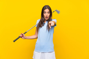 Young golfer woman over isolated yellow wall surprised and pointing front