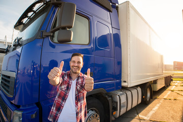 Portrait of happy smiling middle aged truck driver standing by his truck and holding thumbs up....