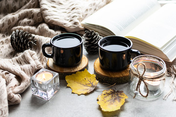 Hygge style autumn composition with two cups of aromatic coffee, warm blanket, autumn decor and interesting book.