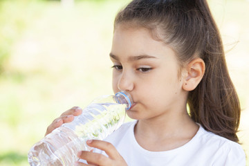 Cute adorable child girl drinking clear water outdoors.