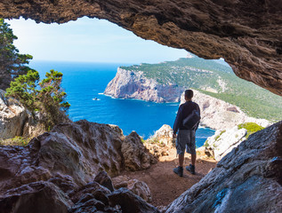 Hiker with backpack by a cave in Capo Caccia