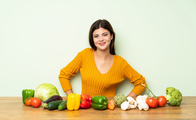 Fototapeta premium Teenager girl with many vegetables posing with arms at hip and smiling