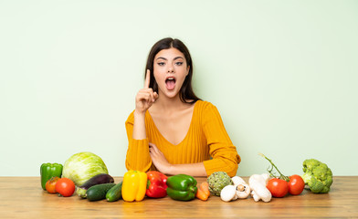 Teenager girl with many vegetables thinking an idea pointing the finger up