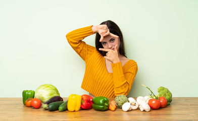 Fototapeta premium Teenager girl with many vegetables focusing face. Framing symbol